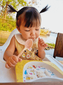 a little girl in a high chair eating rice with a spoon from a plate that says ' oat ' on it