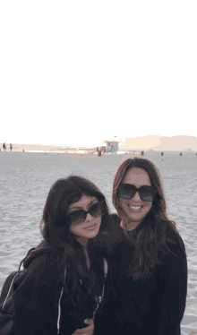 two women wearing sunglasses are posing for a picture on a beach