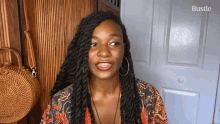 a woman with dreadlocks and hoop earrings is smiling in front of a door with the word bustle on it