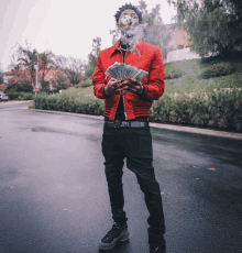 a man in a red jacket holds a stack of money in his hands