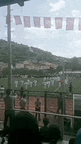 a group of people are standing on a field with flags hanging from a pole with the letter c on them