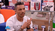 a man with a mustache is sitting in front of a display of kitchen appliances including a pot that says slim