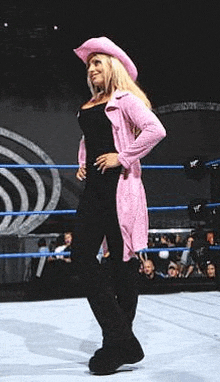 a woman is standing in a wrestling ring wearing a cowboy hat and a pink coat .