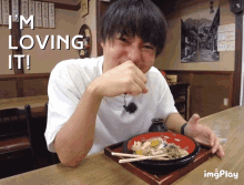 a man is sitting at a table with a bowl of food and the words " i 'm loving it " above him