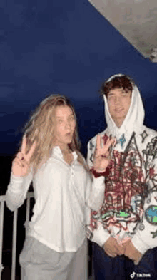 a man and a woman are standing next to each other and making peace signs .