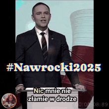 a man in a suit and tie stands at a podium with # nawrocki2025 written on the screen behind him