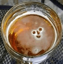 a close up of a glass of beer with a face shaped foam .