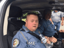 a police officer with down syndrome is sitting in a car holding a bottle of water and says me