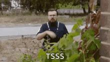 a man with a beard and glasses is standing in front of a plant with the word tsss written on it .