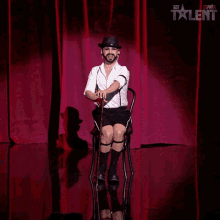 a man is sitting on a chair with a cane in front of a red curtain that says got talent on it