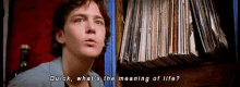 a man is standing in front of a shelf full of records and asking what 's the meaning of life .