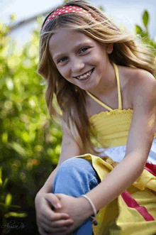 a young girl wearing a yellow top and a red and white headband smiles