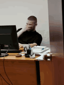 a man sits at a desk covering his face with his hands