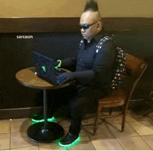 a man with a mohawk is sitting at a table with a laptop and the word sarcasm written above him