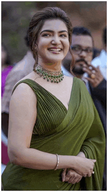 a woman in a green saree and a necklace is smiling .