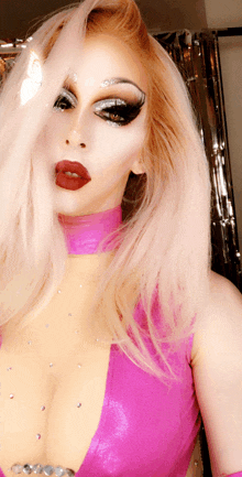 a woman with blonde hair and red lips wearing a pink top