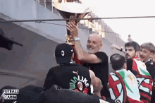 a man in a black shirt that says ' t like ' on it holds a trophy in front of a crowd