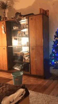 a cat is sitting on top of a wooden cabinet in a living room with a christmas tree in the background .