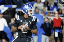 a football player wearing a helmet is holding a football in his hands on a field .