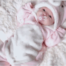 a baby wearing a pink and white outfit with a pacifier in her mouth