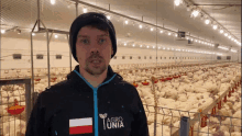 a man in an agro unita jacket stands in front of a chicken coop