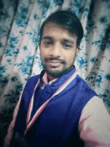 a man with a beard and a medal around his neck is taking a selfie in front of a curtain .