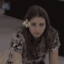 a woman with a flower in her hair is sitting on the floor in front of a sign that says good black friday