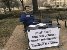 a man sits behind a table with a sign that says change my mind