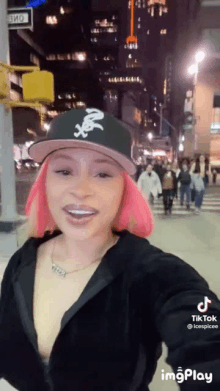 a woman with pink hair is wearing a baseball cap and taking a selfie .