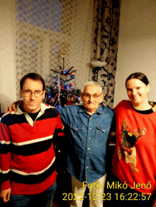 three people posing for a picture with a christmas tree behind them