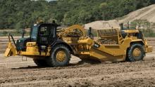 a large yellow cat tractor is driving through a dirt field