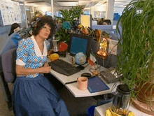 a woman is sitting at a desk with a computer and a cup of tea