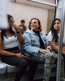 a man in a denim jacket sits with two women on a train