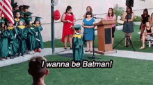 a little boy in a graduation cap and gown is standing in front of a podium and talking to a crowd .