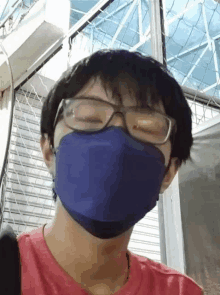 a young man wearing a blue mask and glasses is standing in front of a fence .