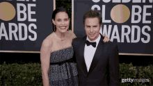 a man and a woman are posing for a picture in front of a sign that says " golden globe awards "