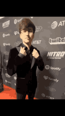 a man in a suit stands on a red carpet sponsored by at & t spotify and nitro