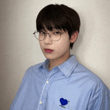 a young man wearing glasses and a blue shirt with a blue heart on the chest