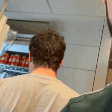 a man standing in front of a fridge filled with coke cans