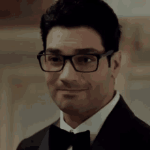 a man wearing glasses and a tuxedo is smiling and making a face .