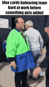 a man in a green jacket and blue apron is standing next to another man .