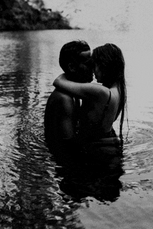 a black and white photo of a man and a woman kissing in the water