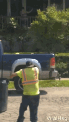 a man in a yellow vest is standing in front of a blue truck that says viralhog on the bottom