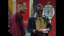 two men are standing next to each other in front of a pool table and talking to each other .