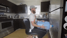 a man sits in a chair in a kitchen holding a blue water bottle with the letter a on it