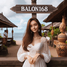 a woman in a white dress stands in front of a wooden sign that says balon168