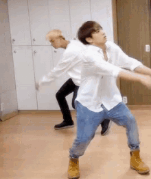 two men are dancing in a room and one is wearing a white shirt and jeans