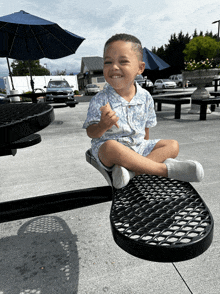 a little boy is sitting on a metal picnic table and smiling