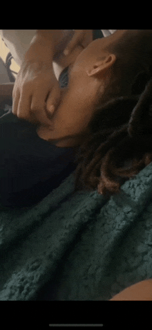 a person with dreadlocks is laying on a bed with a green blanket