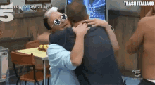 a man wearing sunglasses is hugging another man with trash italiano written on the bottom